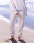 Person wearing a white matching sweat set standing on a beach with ocean waves in the background