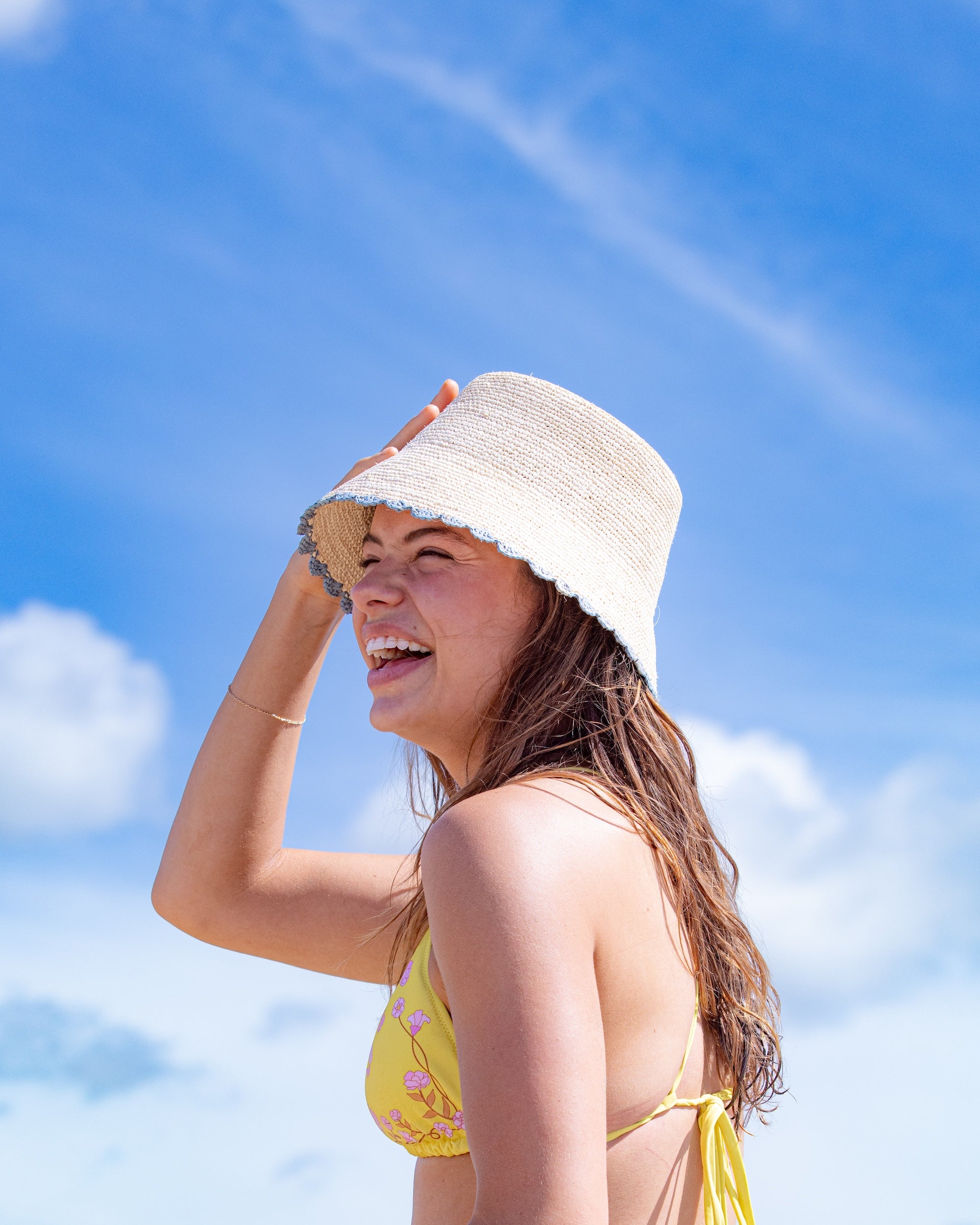 Woman wearing a yellow bikini and white sun hat against a blue sky.