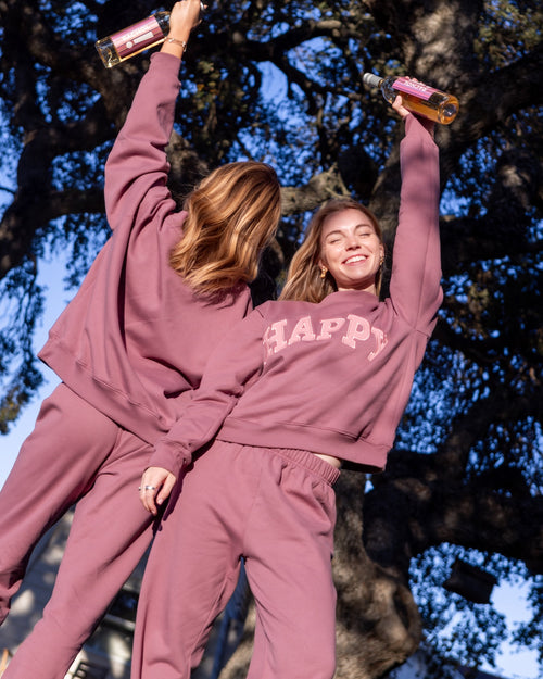 Two people in matching pink 'HAPPY' matching outfits standing outdoors with trees in the background.