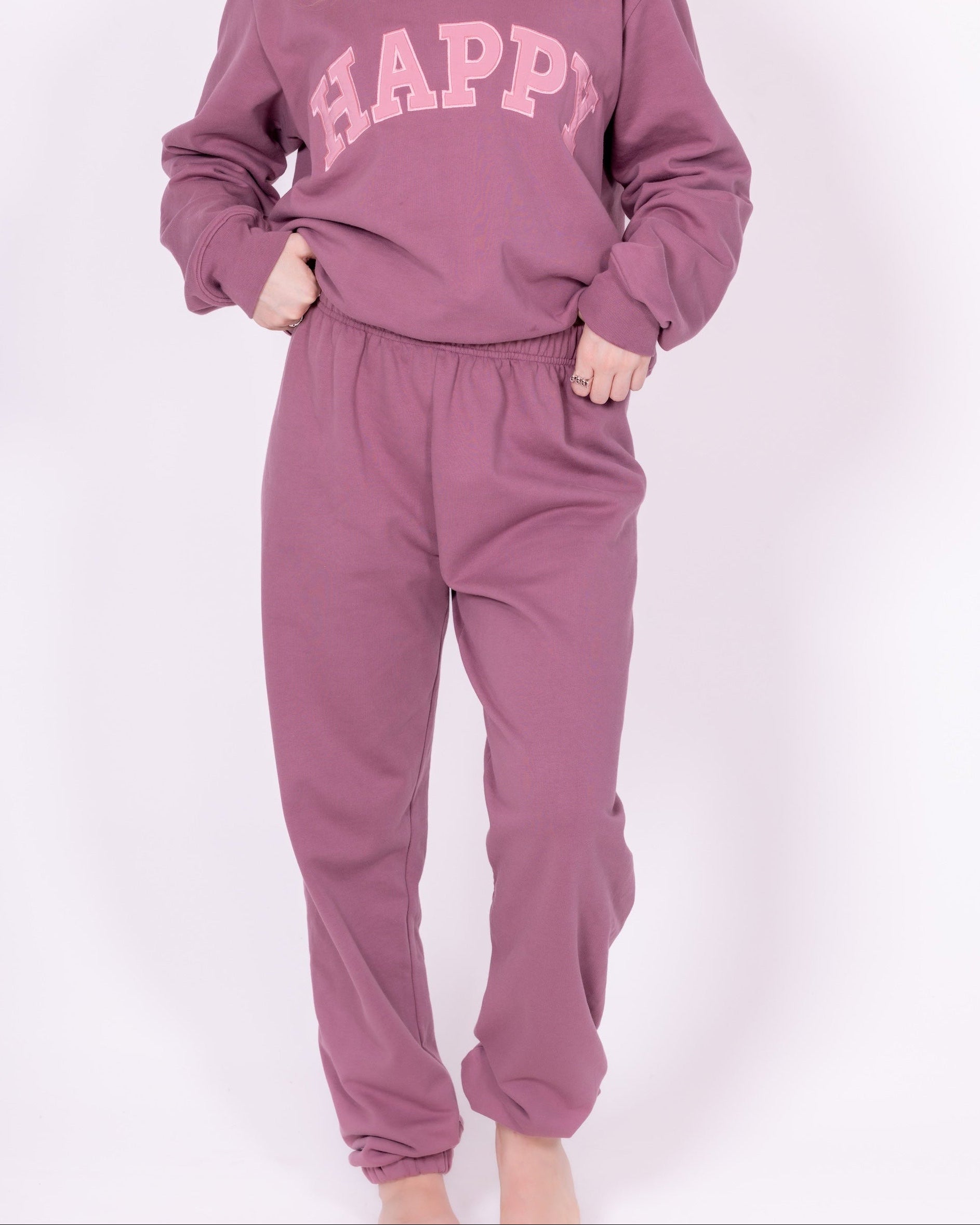 Person wearing a mauve 'HAPPY' sweatshirt and pants on a white background