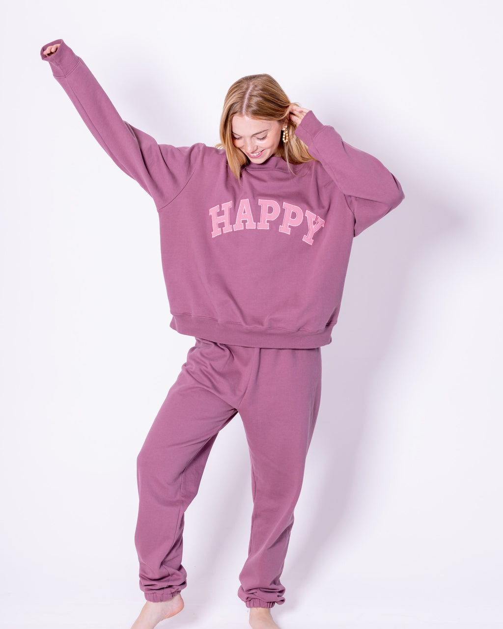 Person wearing a pink and mauve 'HAPPY' sweatshirt and joggers on a white background